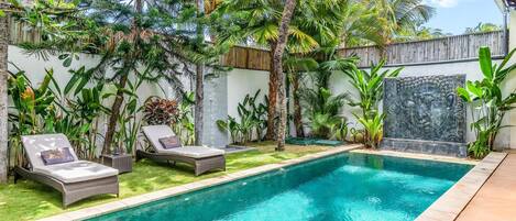 Une piscine dotée de chaises longues et agrémentée de plantes tropicales.