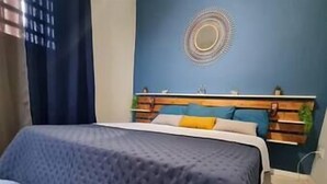 Un llit amb un llençol blau, un capçal de fusta i una paret amb un disseny circular.