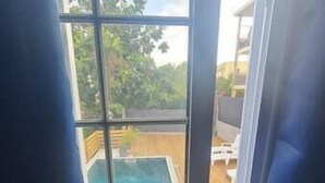 A window with a view of a swimming pool and outdoor furniture. - VBF -studio Pool View (Fort-de-France Bay)