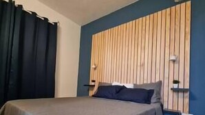 A bedroom with a bed, dark curtains, a wooden headboard, and a blue wall. - VBF -studio Pool View (Fort-de-France Bay)