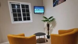 A room with two yellow chairs, a small round table, a potted plant, and a television on the wall. - VBF - Cosy Apartment (Fort-de-France Bay)