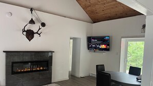 A modern living room with a fireplace, a flat-screen TV mounted on the wall, and a dining area with a table and chairs. - New 2-bedroom cottage in Bancroft Ontario, fully renovated on the lake (MONT)