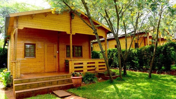 A wooden cabin with a porch, steps leading to the entrance, and a small garden area with a bench and potted plants.