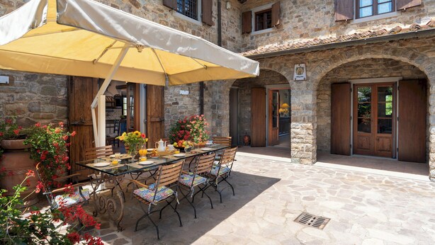 An outdoor patio with a table set for dining, surrounded by stone walls and wooden doors.