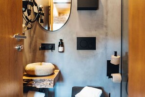 A bathroom with a round stone sink, a mirror, a towel rack, and a toilet paper holder. - a small, very elegant and cosy studio loft of almost 14m2 (Sortelha)