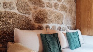 A bed with a stone wall behind it. - a small, very elegant and cosy studio loft of almost 14m2 (Sortelha)