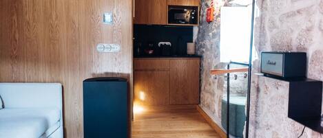 A compact living space with a kitchenette, a compact fridge, a sofa, and a speaker.