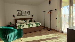 Un dormitorio con cama, una silla verde, una lámpara de pie y una ventana con cortinas.