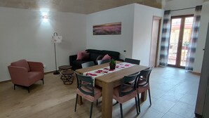 Un comedor con una mesa de madera, sillas rosas, un sofá negro y una mesita redonda con una planta.