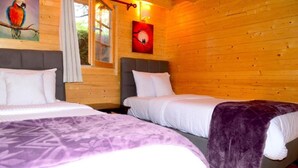 Ein Holzhütten-Zimmer mit zwei Betten, einem Fenster und einem Papageienbild.