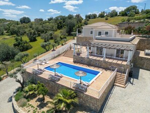 Une villa dotée d’une piscine, de murs en pierre et d’un jardin planté de palmiers.