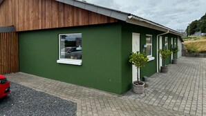 Un edificio verde con techo inclinado, una ventana que muestra un coche y un coche rojo estacionado en la parte delantera.