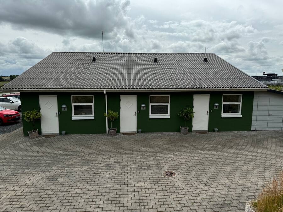 A green building with a tiled roof, numbered doors, and a paved driveway.