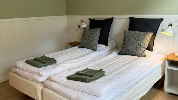 Una cama doble con sábanas blancas, dos toallas verdes y almohadas estampadas.