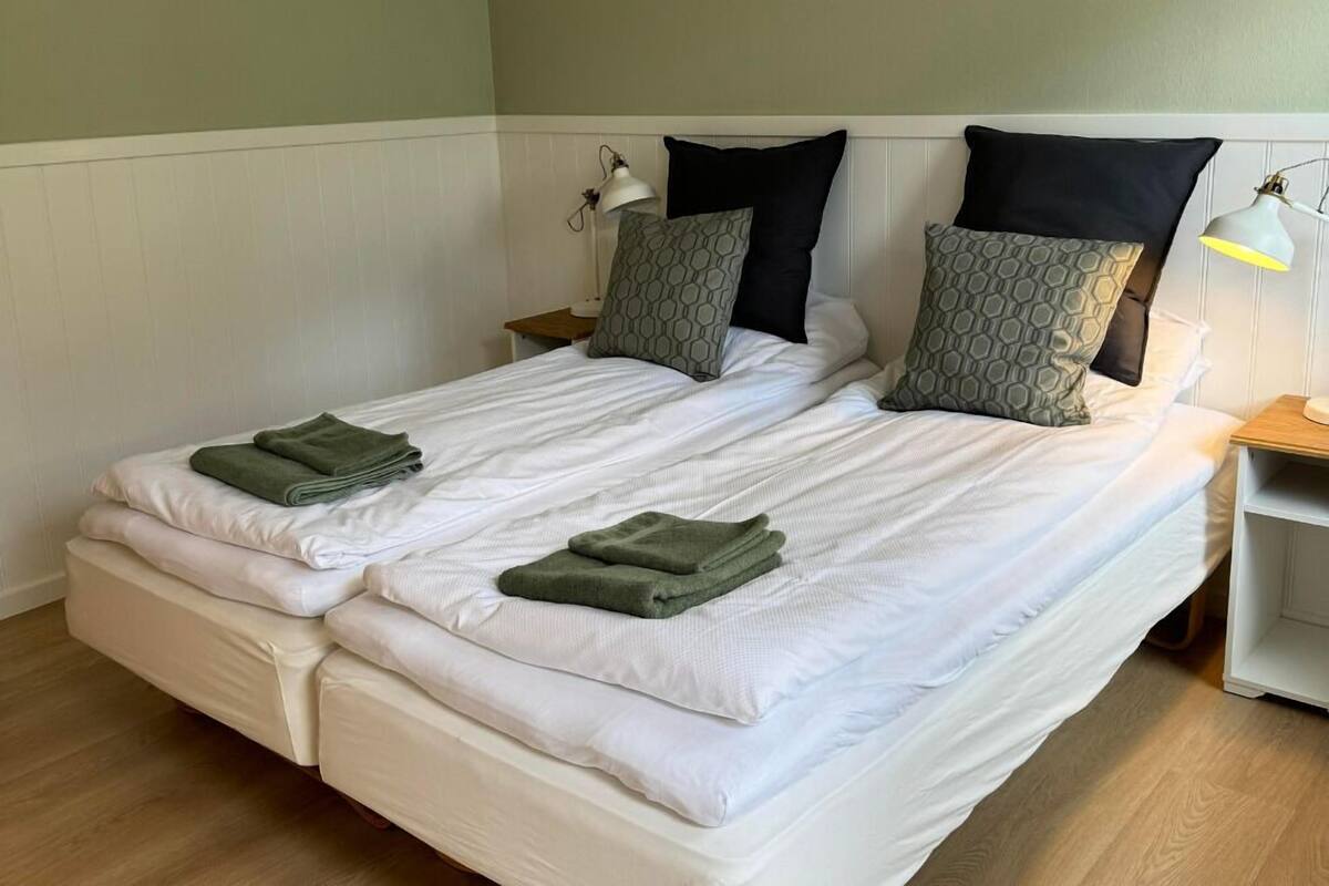 A double bed with white linens, two green towels, and patterned pillows.