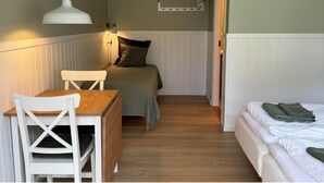 Una habitación pequeña y acogedora con una cama, un escritorio y una silla. Hay un estante sobre la cama y una lámpara colgante.