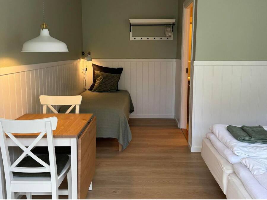 Una habitación pequeña y acogedora con una cama, un escritorio y una silla. Hay un estante sobre la cama y una lámpara colgante.