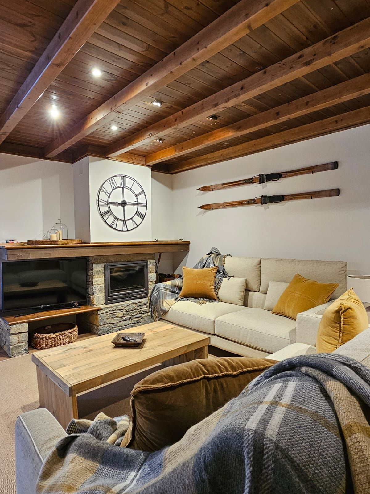 A cozy living room with a stone fireplace, a large wall clock, and skis mounted on the wall.