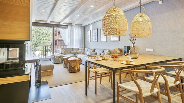 Une cuisine moderne avec un plan de travail en bois, un coin repas avec des chaises en osier et une grande fenêtre donnant sur une zone boisée.