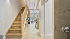 Un escalier en bois menant à un balcon agrémenté de mobilier d’extérieur, une porte dotée d’une poignée moderne et un plafond avec des poutres apparentes.
