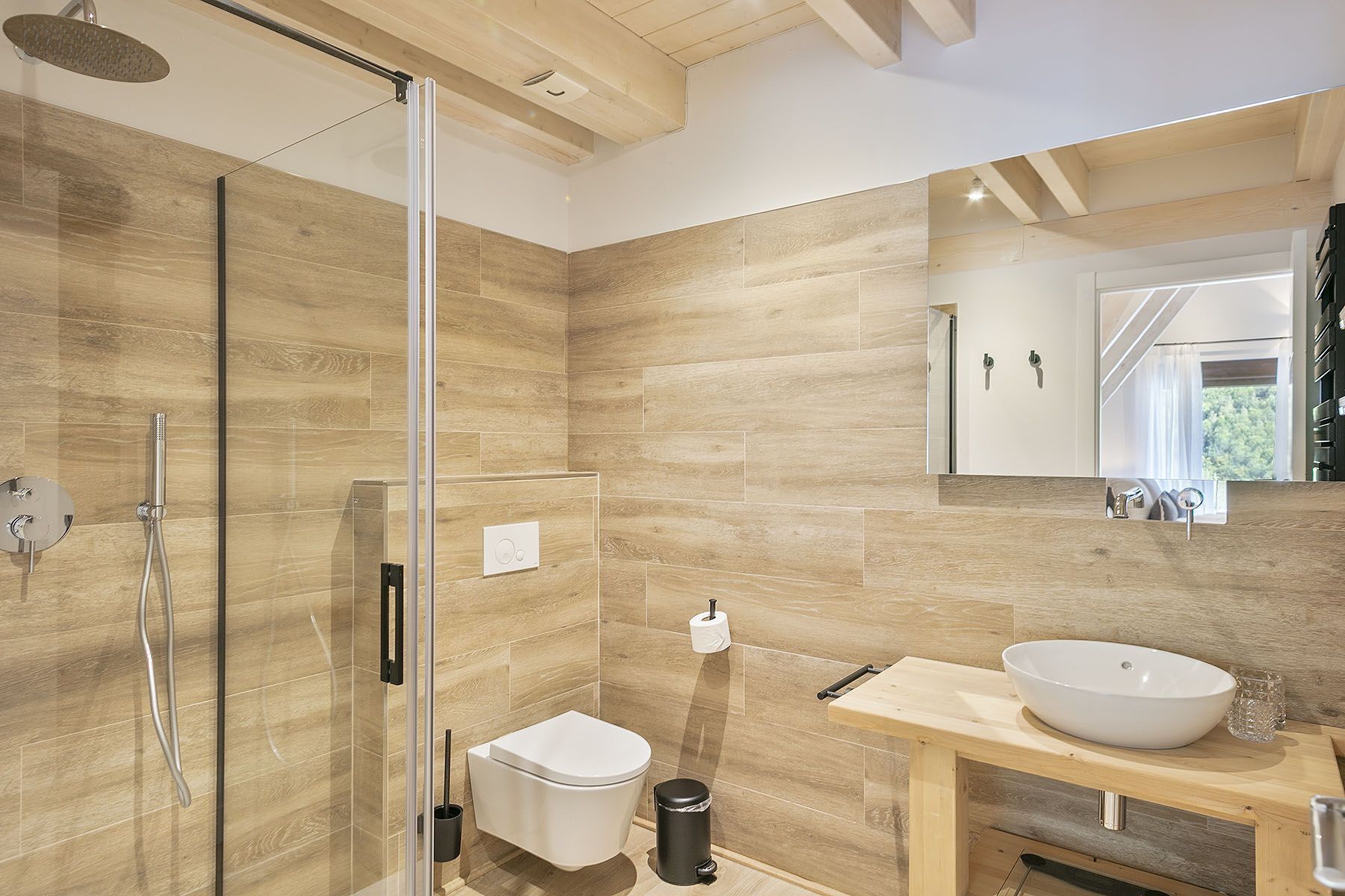 Une salle de bain moderne avec une douche à parois de verre, des toilettes blanches, un meuble-lavabo en bois doté d’un grand évier et un miroir au-dessus du meuble-lavabo.