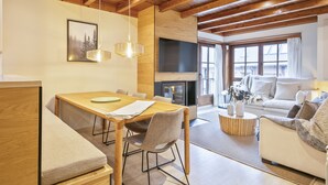 A modern living room with a wooden ceiling, a fireplace, a dining area with a table and chairs, and a sofa. - Luderna - Apartamento Val de Ruda B92 Ticolet (Baqueira)