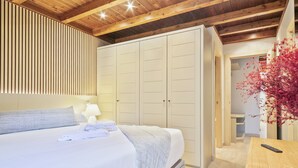 A bedroom with a bed, bedside table, lamp, wardrobe, and a view of a hallway with a plant. - Luderna - Apartamento Val de Ruda B92 Ticolet (Baqueira)