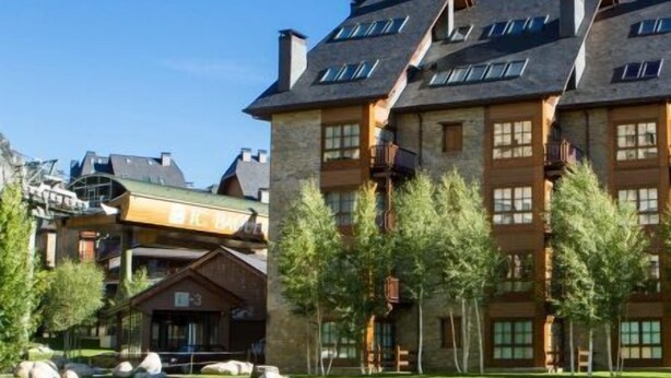 A multi-story building with a stone facade, large windows, and a well-maintained lawn with rocks. - Luderna - Apartamento Val de Ruda B92 Ticolet (Baqueira)