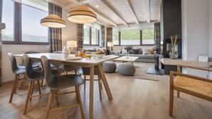 A modern living room with a dining area, wooden flooring, large windows, and a fireplace. - Luderna - Tríplex Amitges (Bagergue)