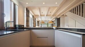 A modern kitchen with a central island, large windows, and a wooden staircase. - Luderna - Tríplex Amitges (Bagergue)