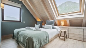 A modern bedroom with a sloped ceiling, a large bed with green bedding, a wooden desk, and a view of a mountain through a skylight. - Luderna - Tríplex Amitges (Bagergue)