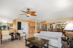 A spacious living area with a white sofa, a glass coffee table, and a ceiling fan. - Wailea Elua Village | Ocean View 2 BR | Car Incl. w/ 6+ Nights | WEV-2009 by KBM (Wailea)