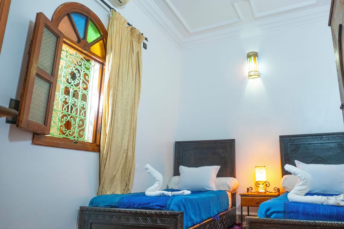 A room with two beds, a stained glass window, and a wall-mounted light fixture.