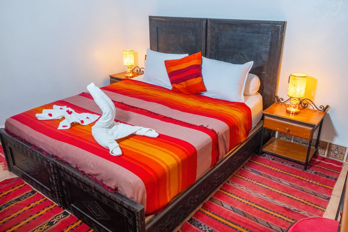 A bed with a striped bedspread, a white towel, and two pillows. There are two bedside tables with lamps.