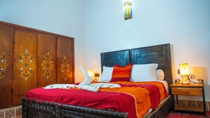 A hotel room with a large wooden wardrobe, a bed with a red and orange bedspread, white pillows, and two bedside lamps. - Riad Taghazoute (Marrakech)