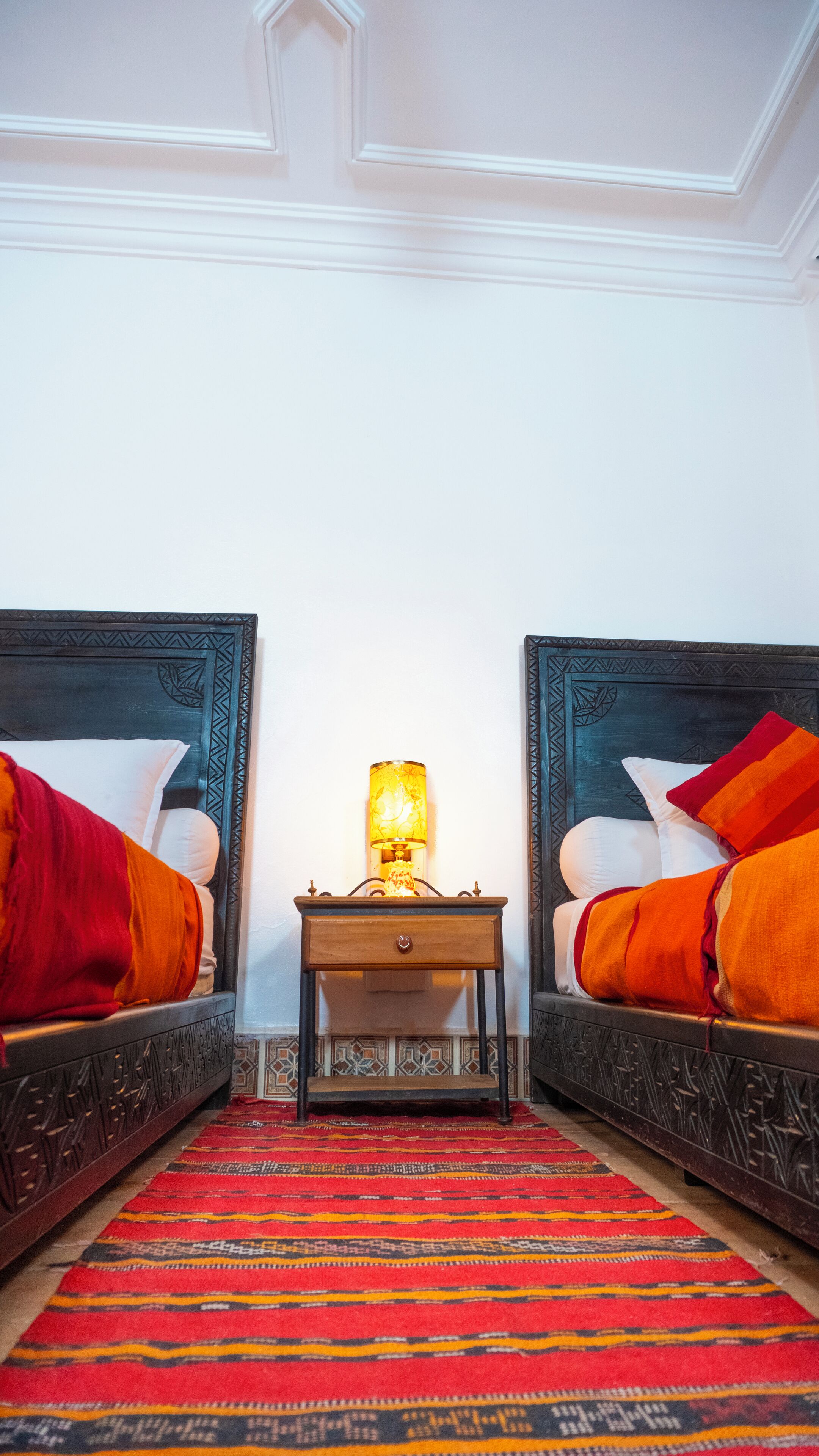A hotel room with two beds, a nightstand with a lamp, and a patterned carpet.