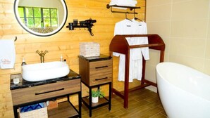 A wooden cabin bathroom with a round mirror, a sink, a vanity, a wooden shelf, a hanging towel rack, and a bathtub.
