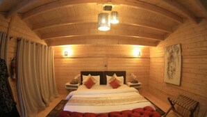 A cozy wooden room with a large bed, two bedside tables, and a red upholstered bench.