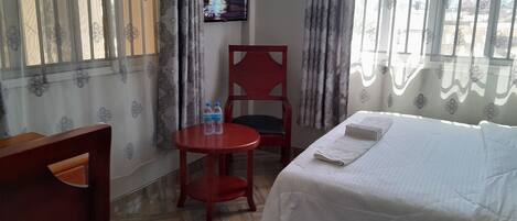 Una habitación de hotel con una cama, un escritorio, una silla y una mesita con dos botellas.