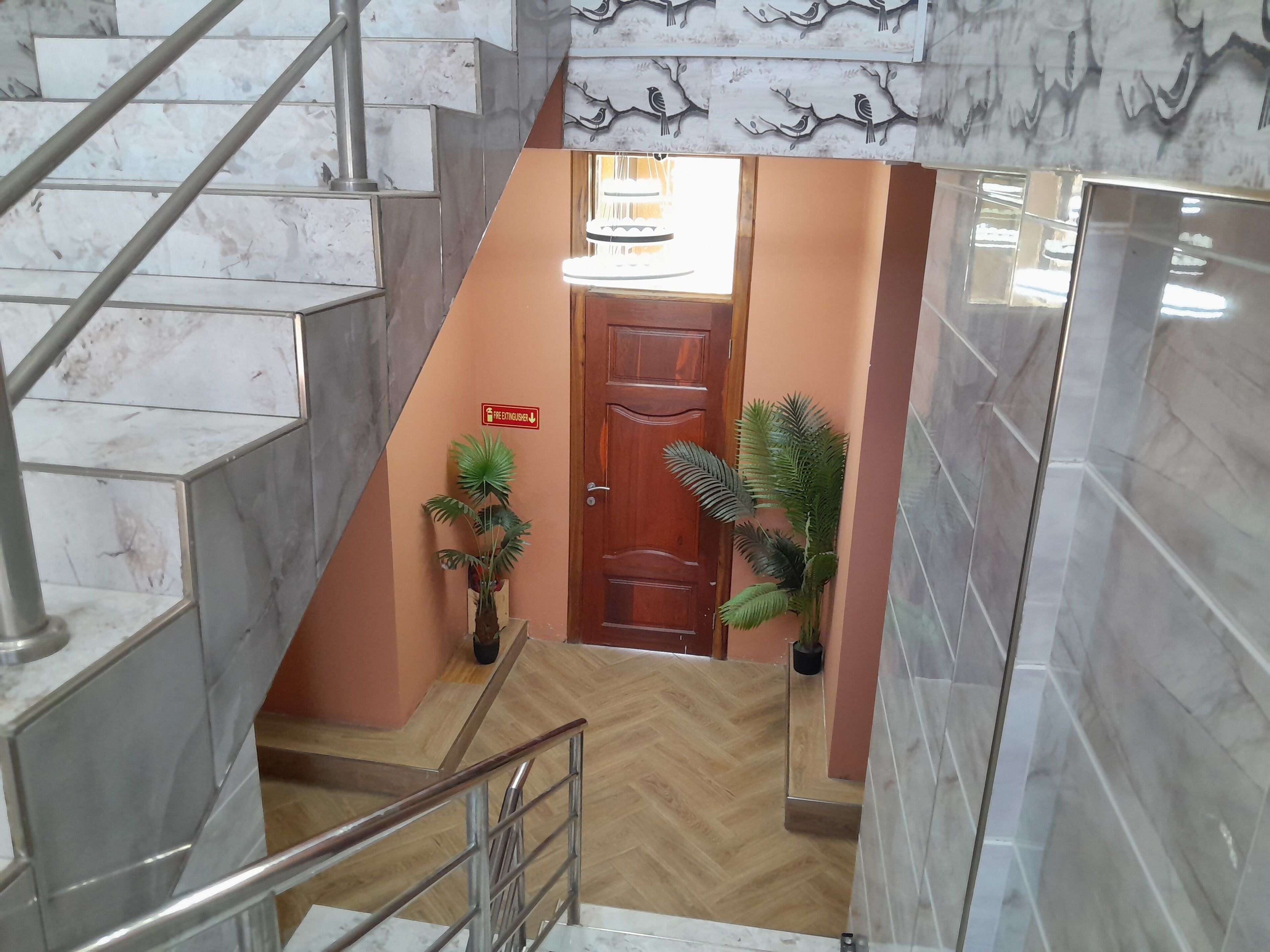 A staircase with marble steps and metal railings, leading to a wooden door with a fire extinguisher sign.