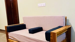 Un sofá de madera con un cojín de color claro y almohadas oscuras, ubicado frente a una pared con toma de corriente.