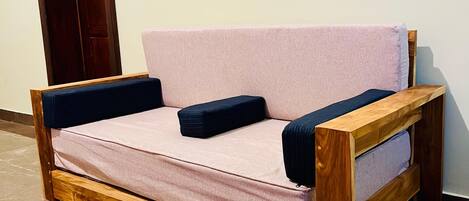 Un sofá de madera con un cojín de color claro y almohadas oscuras, ubicado frente a una pared con toma de corriente.