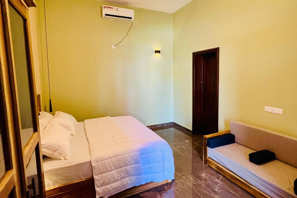 A room with a bed, a sofa, a mirror, an air conditioning unit, and a door.
