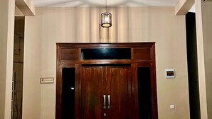 Una habitación con un armario de madera grande, dos sillas, una lámpara colgante y una planta pequeña.