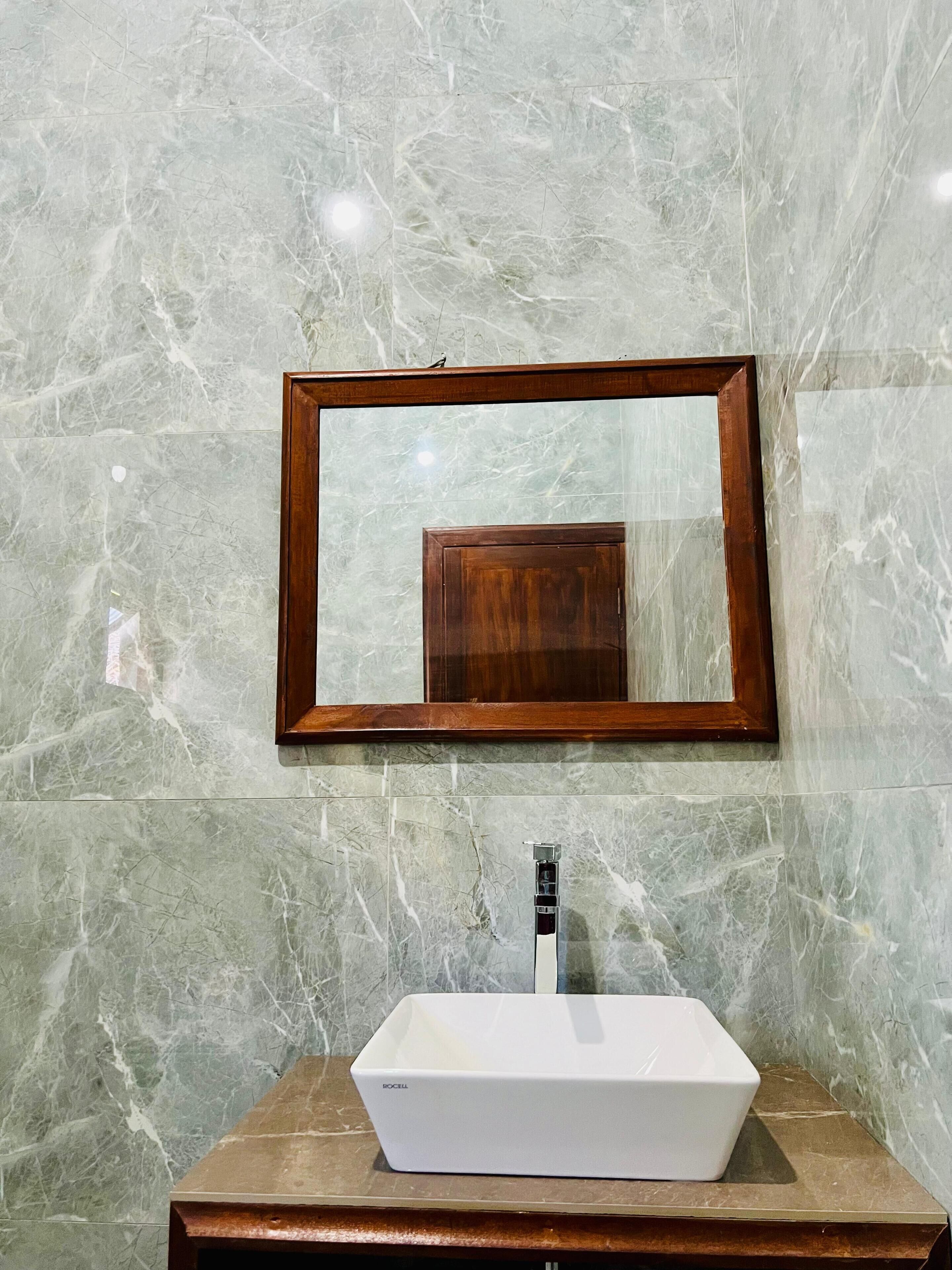 A bathroom with a marble wall, a wooden-framed mirror, and a white sink with a modern faucet.