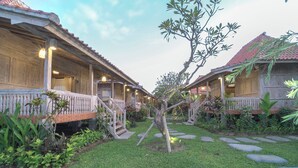 A traditional wooden building with a tiled roof, a small garden with stepping stones, and a tree in the center. - Kirani Joglo (Celuk)