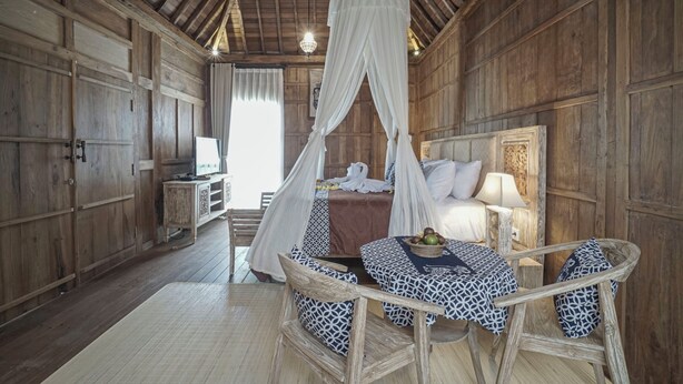 Una habitación de madera con una cama bajo un dosel, una mesa con sillas y un televisor sobre una mesita auxiliar.