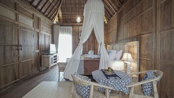 A wooden room with a bed under a canopy, a table with chairs, and a television on a side table.