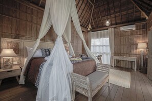 A wooden room with a four-poster bed, a nightstand, a bench, and a table. - Kirani Joglo (Celuk)