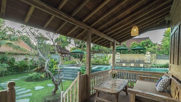 A wooden deck with a table and bench, overlooking a garden with a stone pathway and a pool area.
